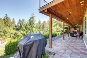 Een overdekt terras met een barbecue, houten balken en uitzicht op een bos.