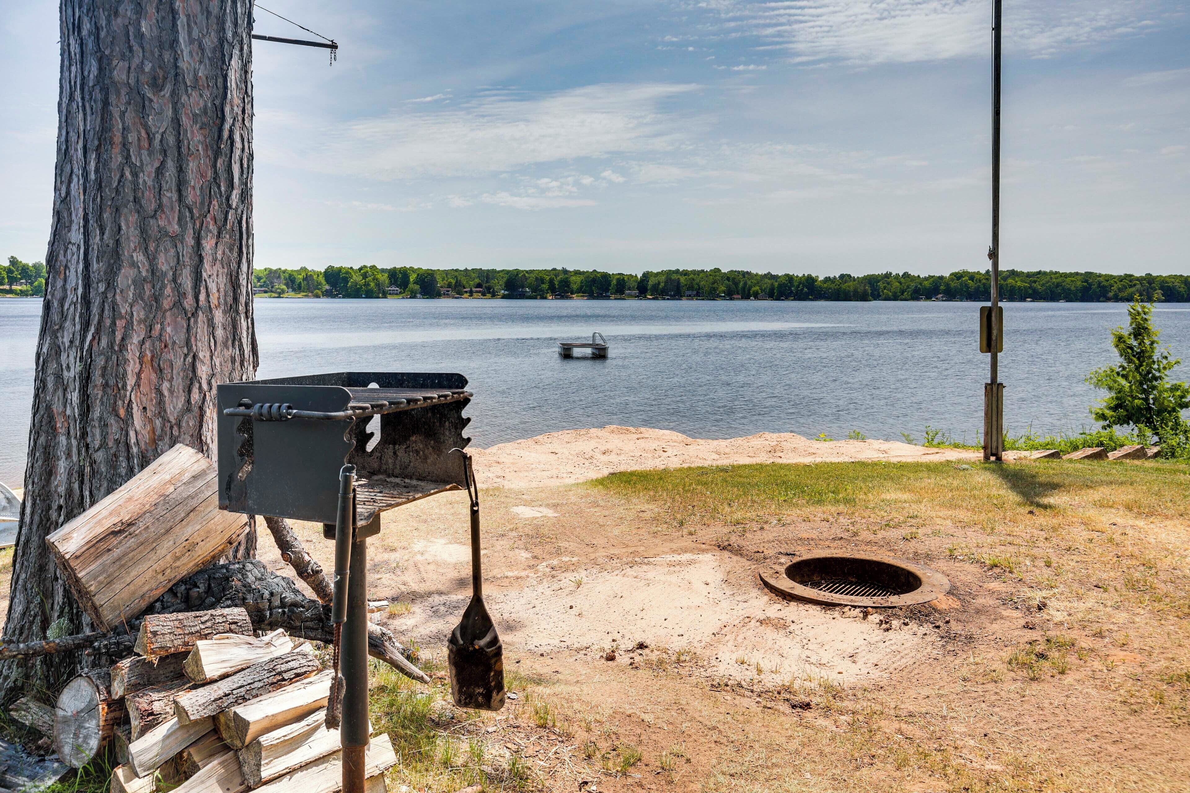 A lakeside camping area with a grill, fire pit, and a boat on the water.