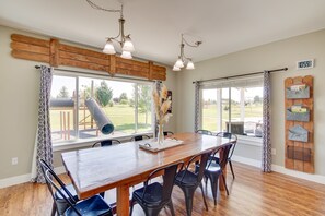 Un comedor con mesa y sillas de madera, ventanas amplias con cortinas y vistas al exterior.
