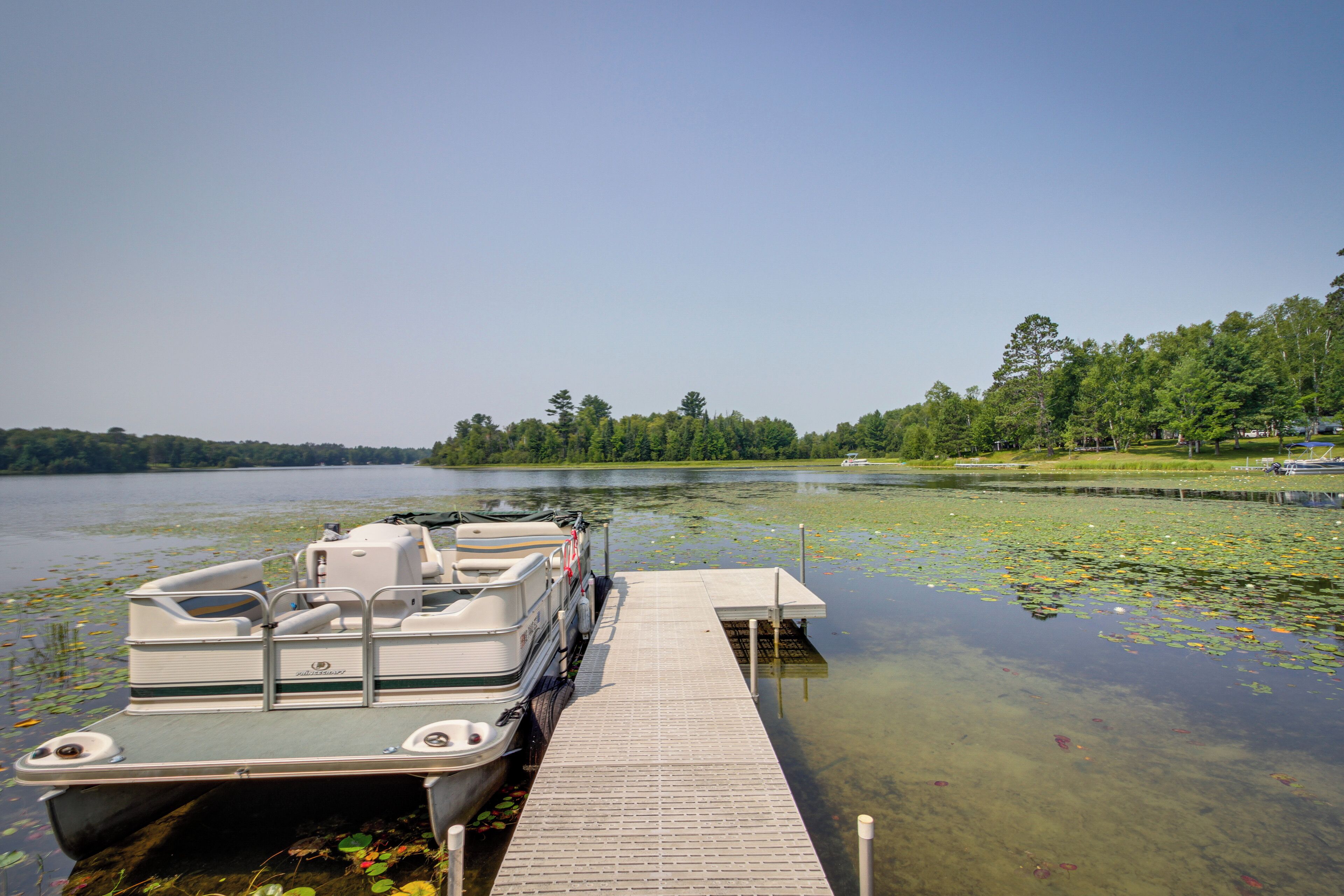 A boat docked at a pier with a clear lake and forested shoreline in the background.