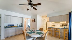 A modern kitchen with a dining area, featuring a round table with chairs, a ceiling fan, and light-colored cabinetry.