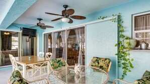A dining area with a round glass table, wicker chairs, and ceiling fans.