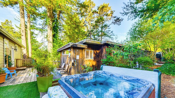 Un jacuzzi en un patio trasero con una terraza de madera, un cobertizo pequeño y una casa al fondo.
