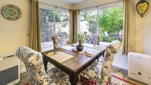 Un comedor con una mesa de madera, sillas con estampado floral, una planta en maceta y un plato decorativo en la pared.