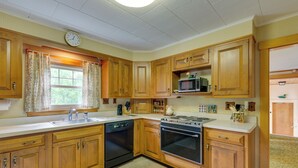 A kitchen with wooden cabinets, a dishwasher, an oven, a microwave, and a clock on the wall. - Cape House in Farmington w/ Shared Outdoor Pool! (Farmington)