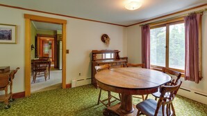 A dining room with a wooden table and chairs, a chandelier, and a view of trees through the window. - Cape House in Farmington w/ Shared Outdoor Pool! (Farmington)