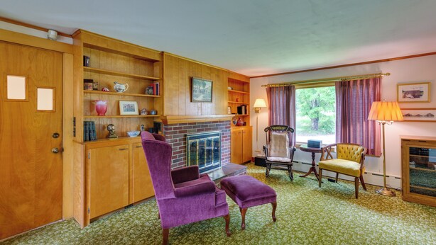 A room with a fireplace, wooden shelves, a purple armchair, a yellow armchair, and a green carpet. - Cape House in Farmington w/ Shared Outdoor Pool! (Farmington)