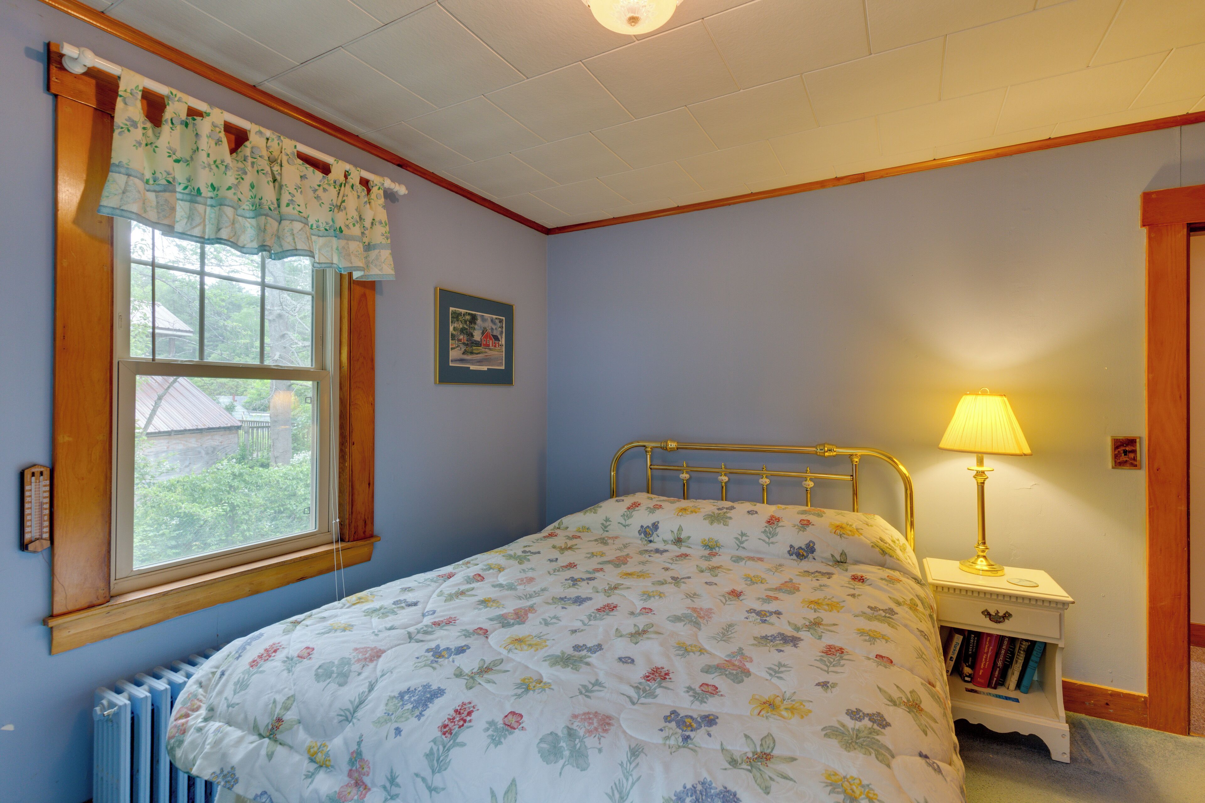 A bedroom with a bed, a window with a view, a bedside table with a lamp, and a radiator.