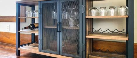 A wooden cabinet with mesh doors and shelves, containing glass jars and bottles.