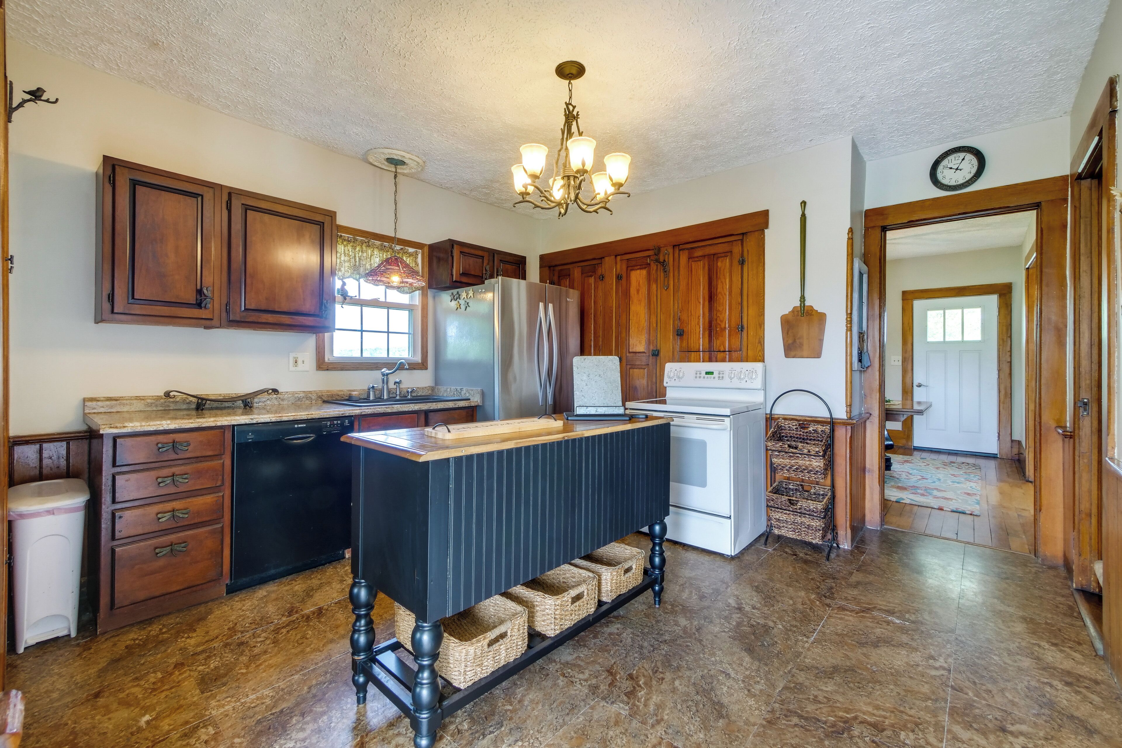 A kitchen with wooden cabinets, a stainless steel refrigerator, a white stove, and a black island with baskets underneath.