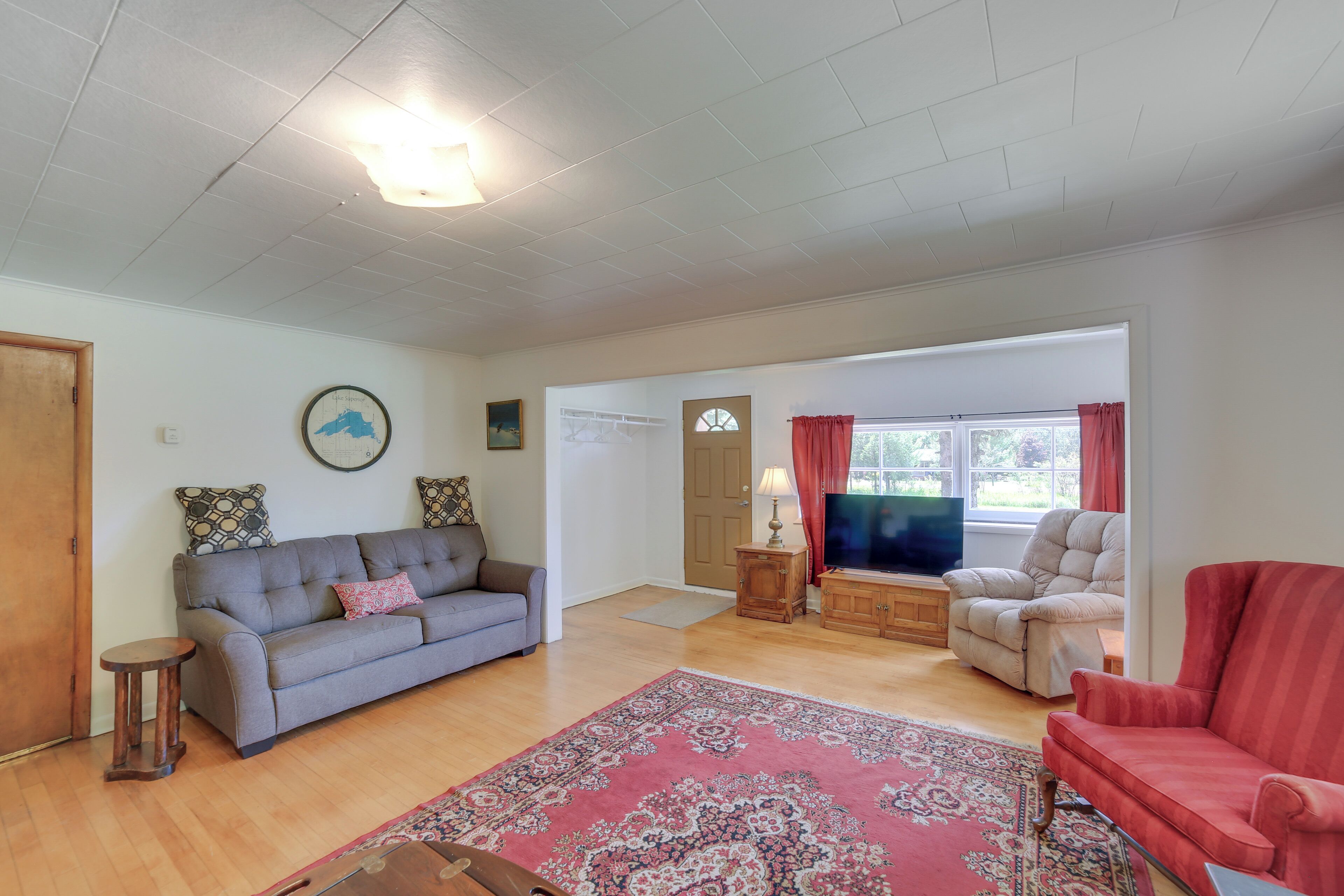 Una sala de estar con un sofá gris, un sillón rojo, un aparador de madera y un televisor.