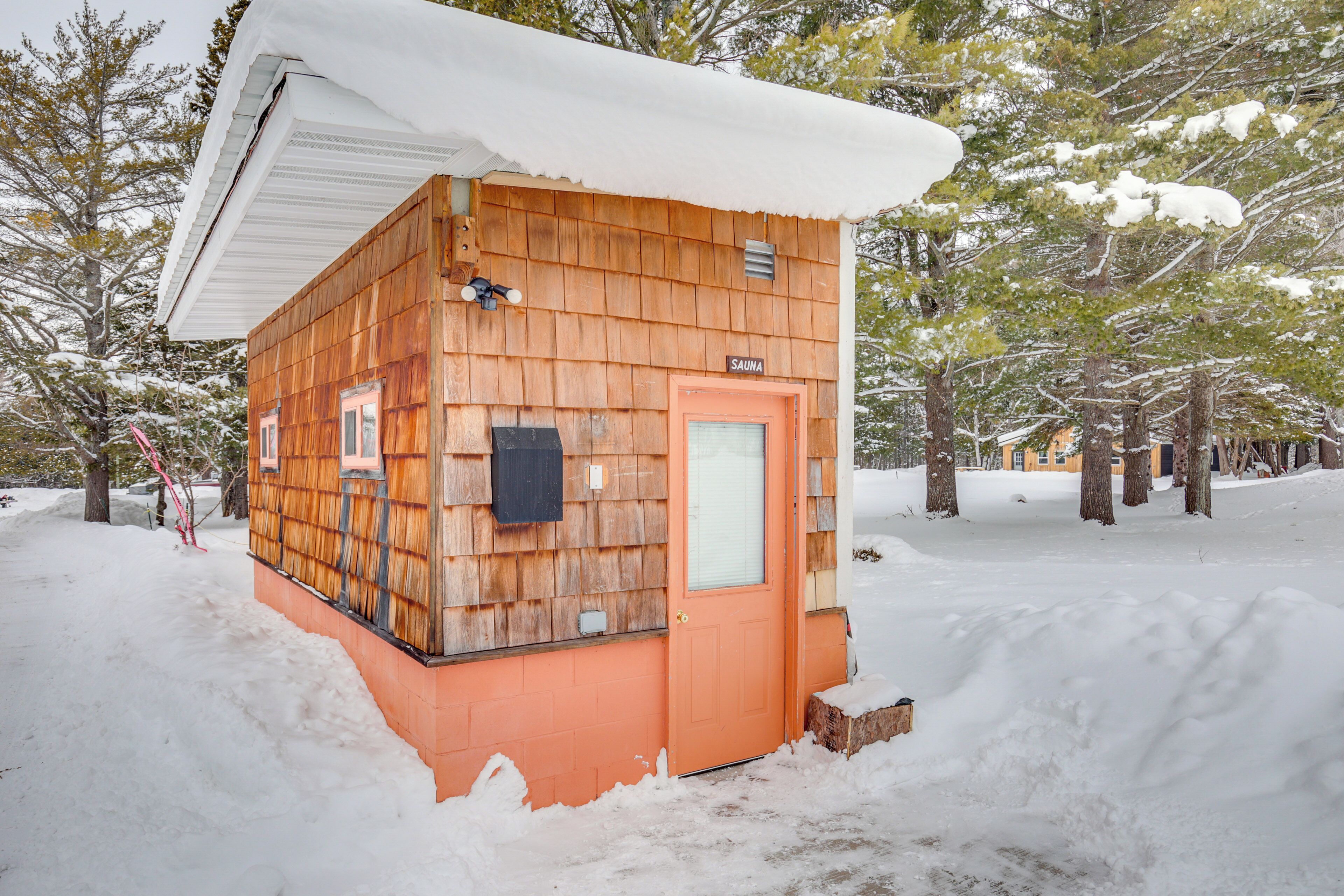 A wooden cabin with a sauna sign, surrounded by snow and trees.