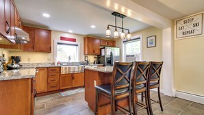 A modern kitchen with wooden cabinets, granite countertops, and a central island with bar stools. - Vermont Vacation Rental: Hot Tub, Near Ski Resorts (Mount Holly)