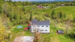 A large house with a red barn, surrounded by a green field and trees. - Vermont Vacation Rental: Hot Tub, Near Ski Resorts (Mount Holly)