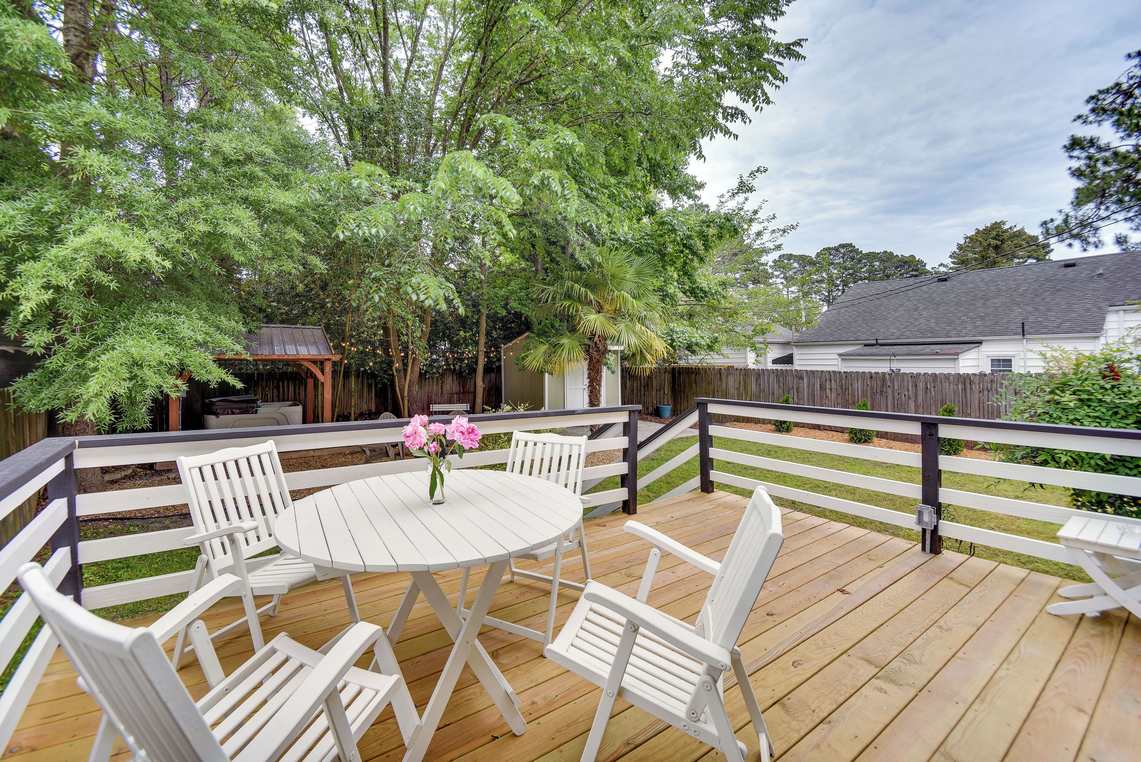 A wooden deck with white chairs and a table, surrounded by trees and a wooden fence.