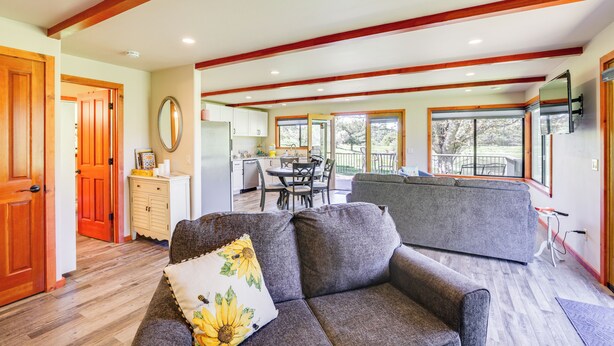 A spacious living area with a grey sofa, wooden beams on the ceiling, a dining table with chairs, and large windows offering a view of the outdoors. - Julian Cottage Stay w/ Near Wildlife & Wineries (Julian)