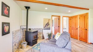 A cozy living room with a stone fireplace, a gray sofa, wooden doors, and a framed picture of a bird. - Julian Cottage Stay w/ Near Wildlife & Wineries (Julian)
