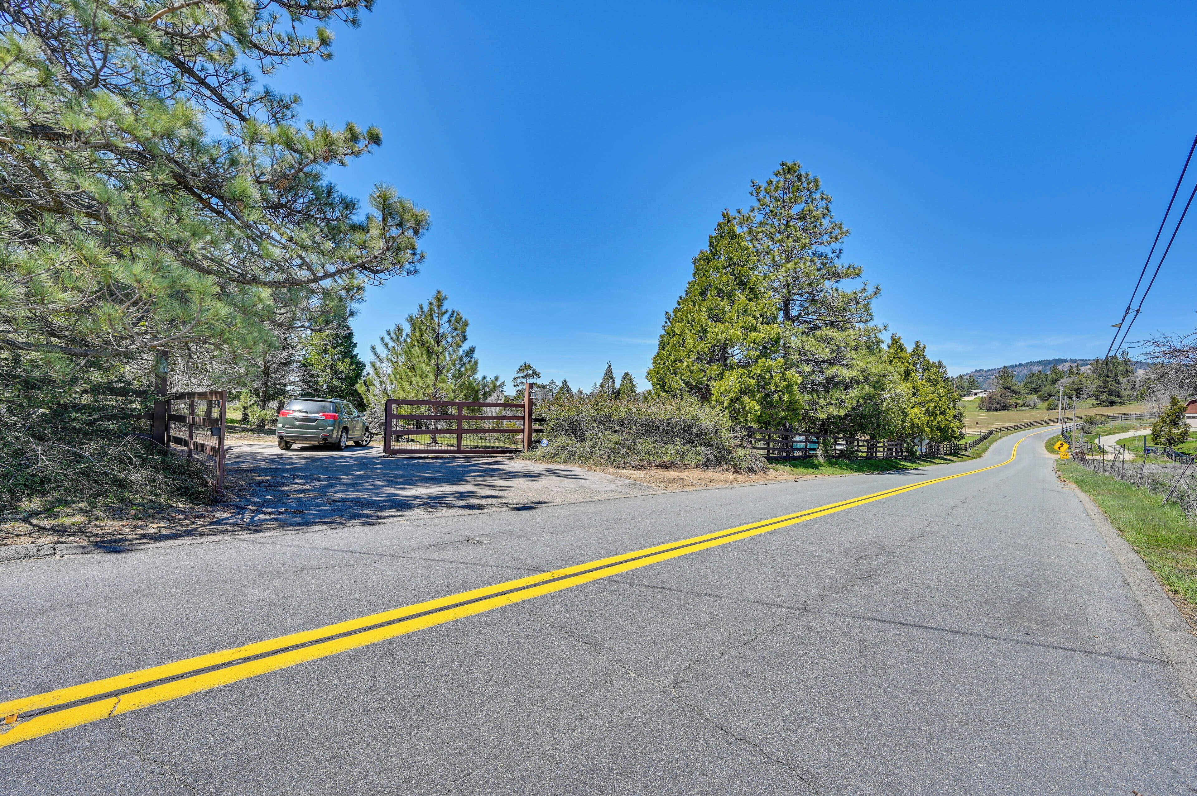 A paved road with double yellow lines, flanked by trees and a wooden gate.