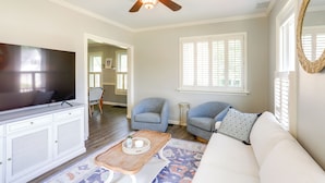 A living room with a ceiling fan, a flat-screen TV, a white sofa, two armchairs, a coffee table, and a patterned rug. - Vermilion Home - Walk to Main Street Beach! (Vermilion)