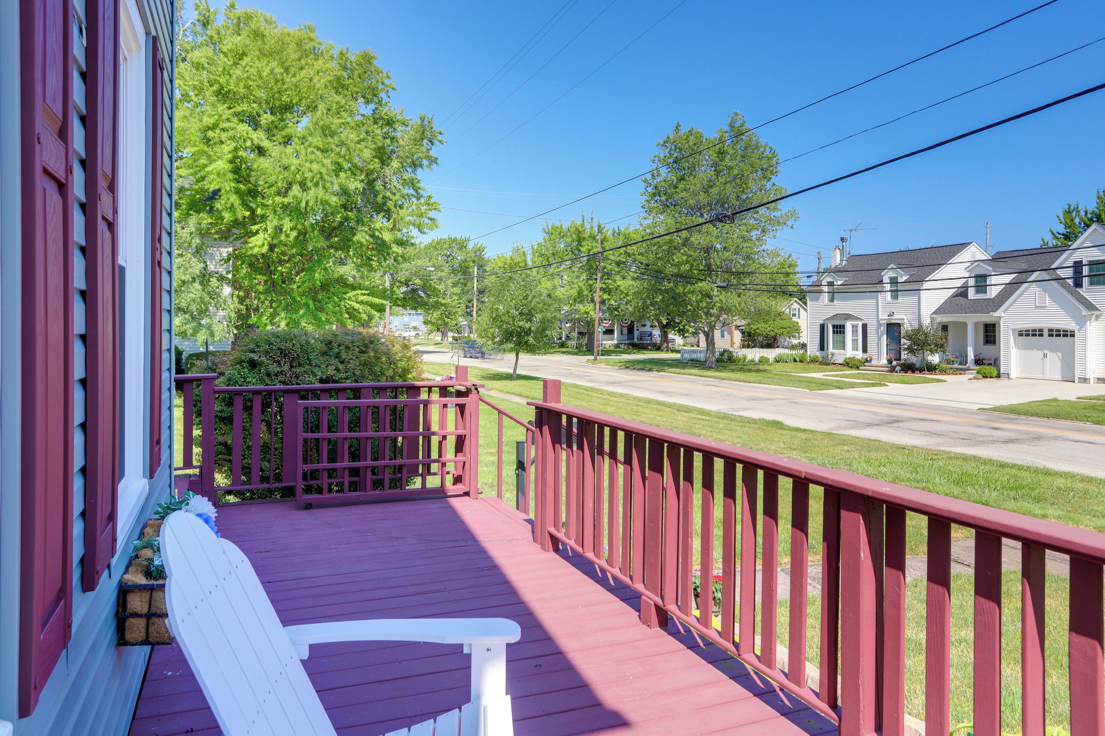 A porch with a red railing, a white bench, and a view of a residential street with houses.