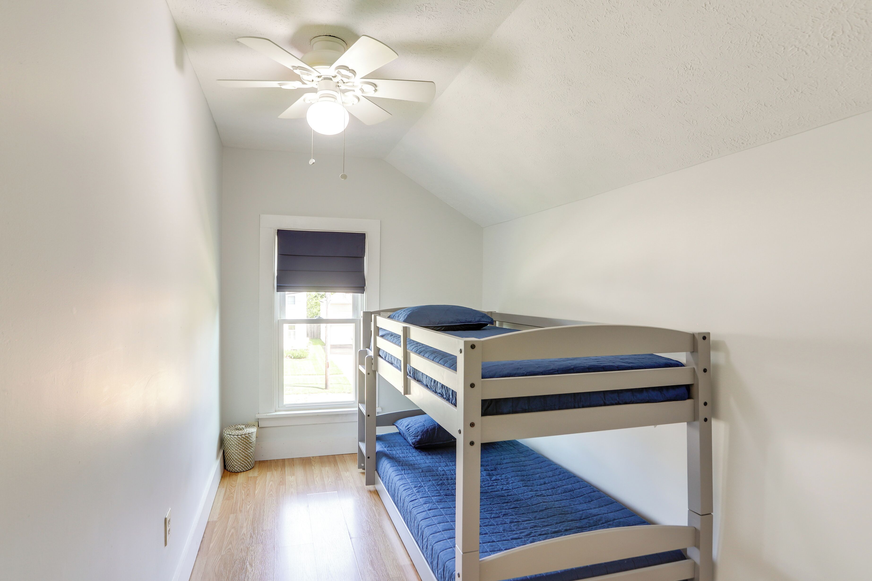 Ein Schlafzimmer mit Etagenbetten, Deckenventilator, Fenster mit Jalousien und einer Tür.