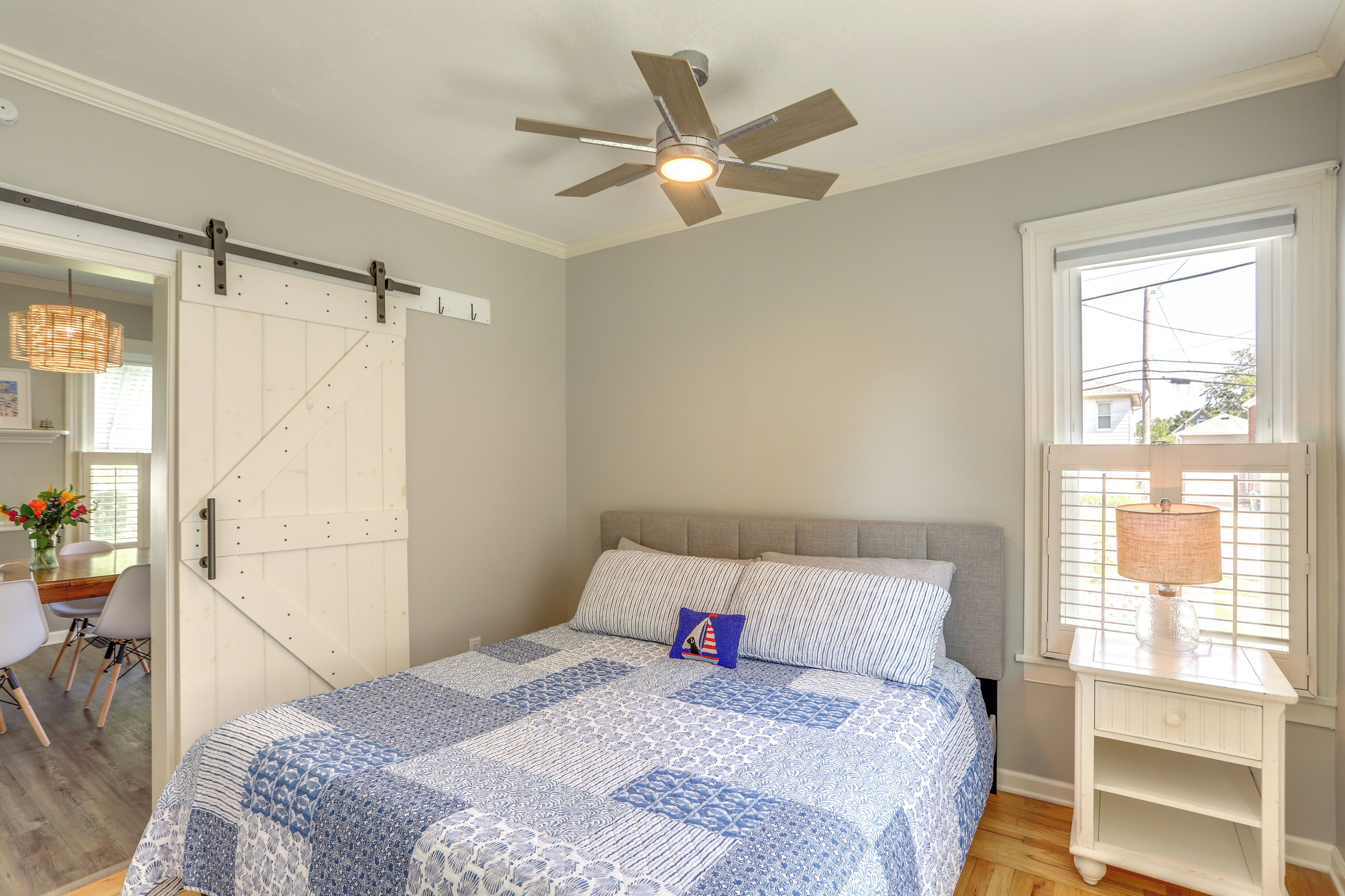 Une chambre à coucher avec un lit, un ventilateur de plafond, une fenêtre avec des stores et une table de chevet avec une lampe.