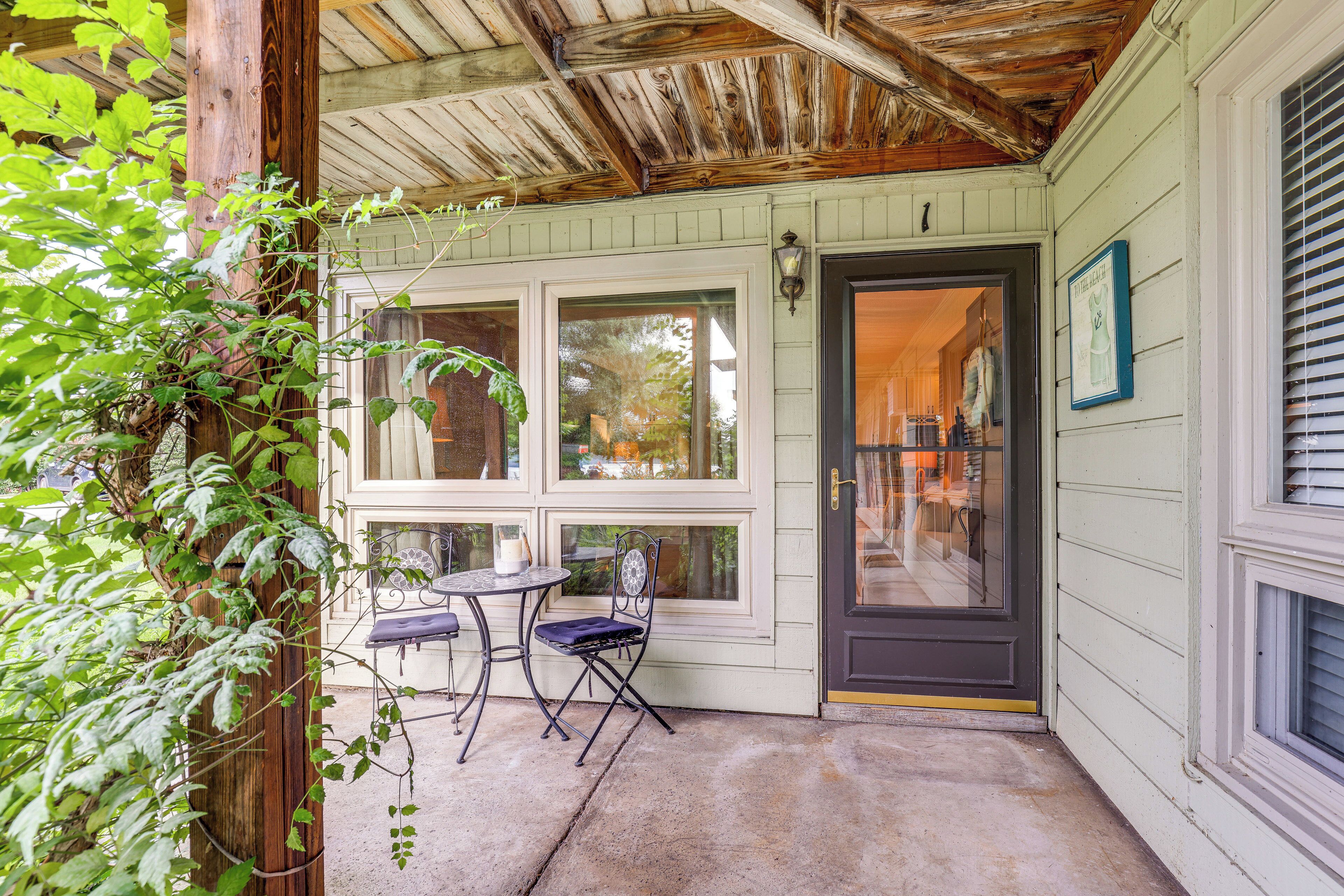 A covered porch with a table and chairs, a door leading inside, and a window with a view of the outside.
