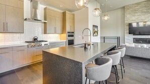 A modern kitchen with a central island, bar stools, stainless steel appliances, and pendant lighting.