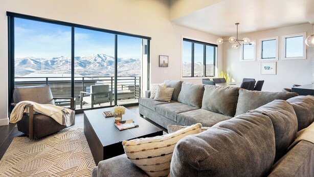 A modern living room with a large gray sectional sofa, a coffee table, and a view of mountains through large windows.