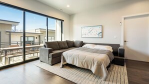 A modern bedroom with a large bed, a sofa, and a view of a balcony with outdoor seating.