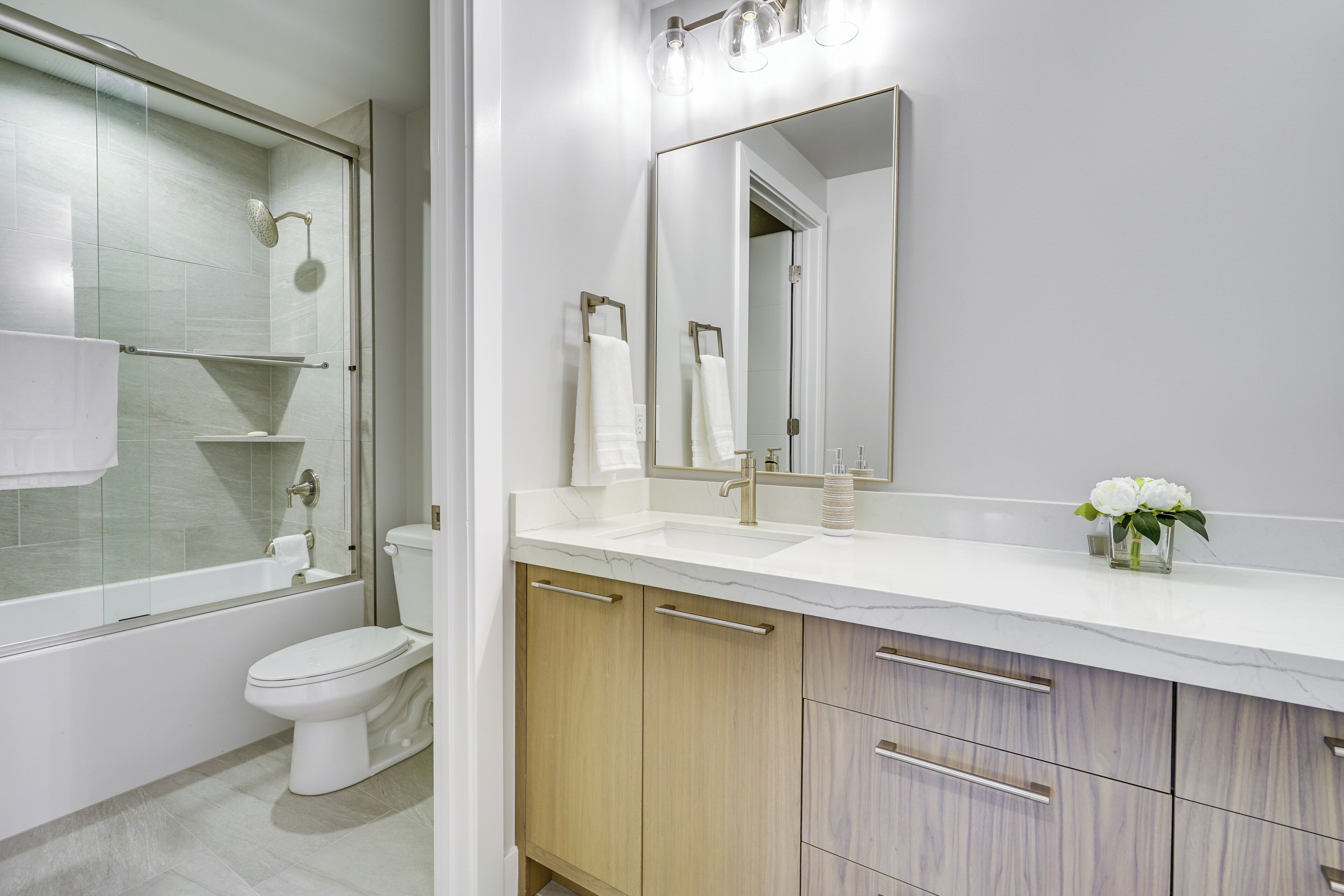A modern bathroom with a glass-enclosed shower, a white toilet, a marble countertop, and wooden cabinets.