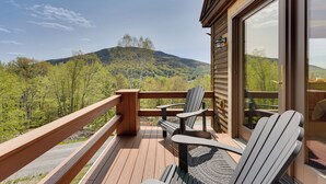 A wooden deck with Adirondack chairs and a glass door leading to a mountain view.