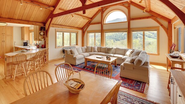 A spacious living area with a large wooden ceiling, a built-in kitchen, and a view of the outdoors.