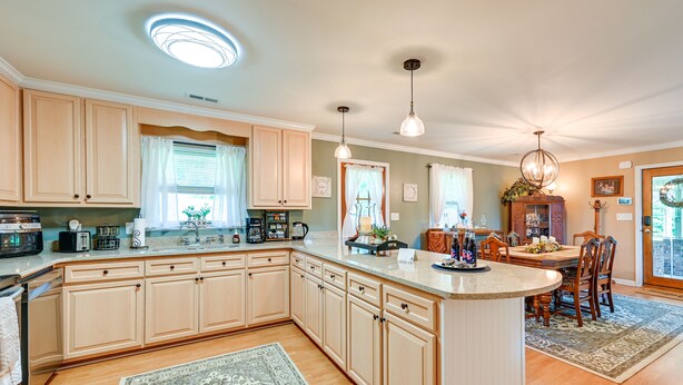 A spacious kitchen with light wood cabinets, a large island, and a dining area with a wooden table and chairs. - 'the Travis House at Lantern Springs' on Farm! (Lexington)