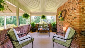 A covered patio with brick walls, two green patterned chairs, a table with a vase and candles, and hanging plants. - 'the Travis House at Lantern Springs' on Farm! (Lexington)