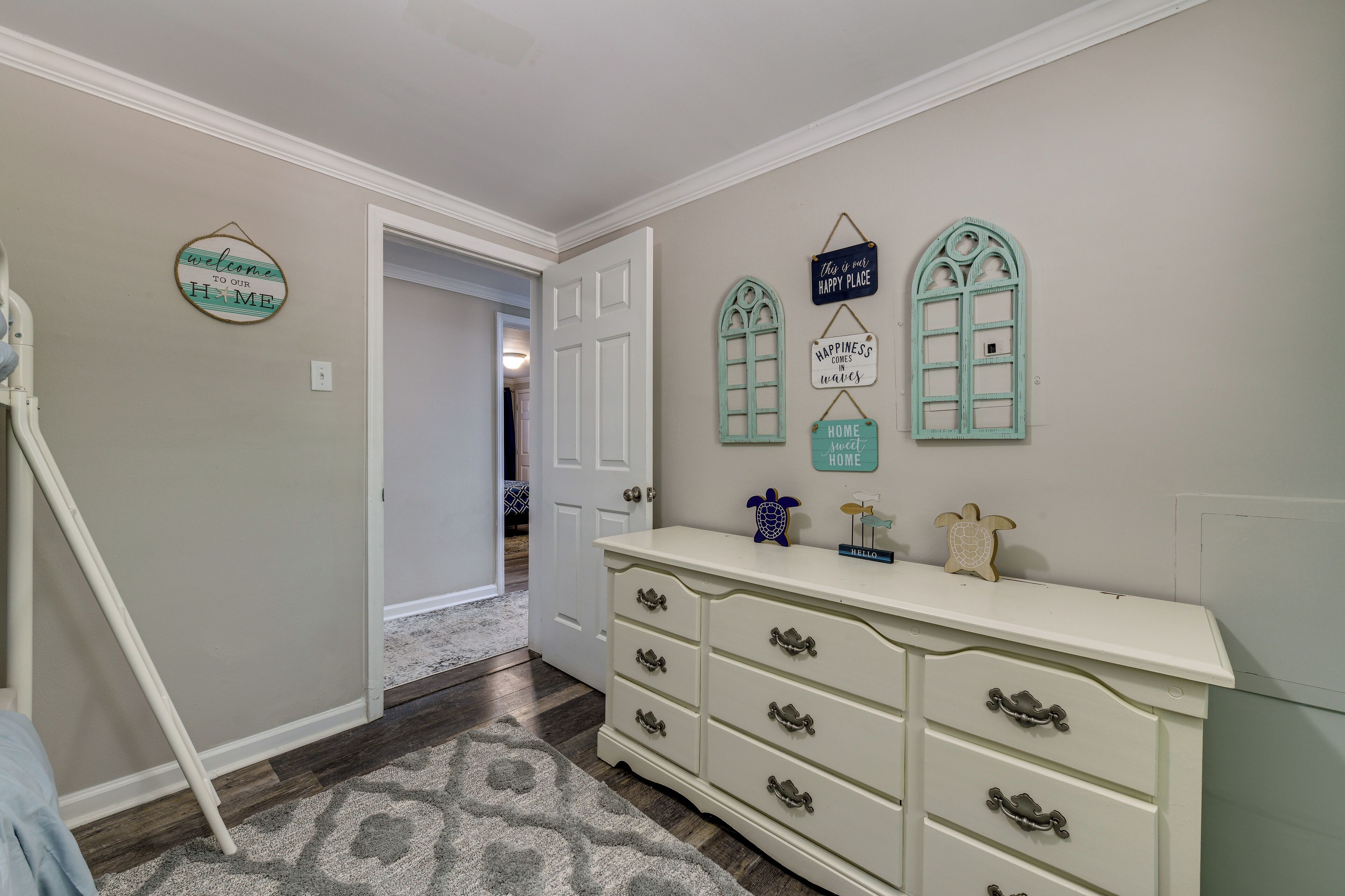Een gang met een witte dressoir, een welkomstbord en decoratieve raamstickers.