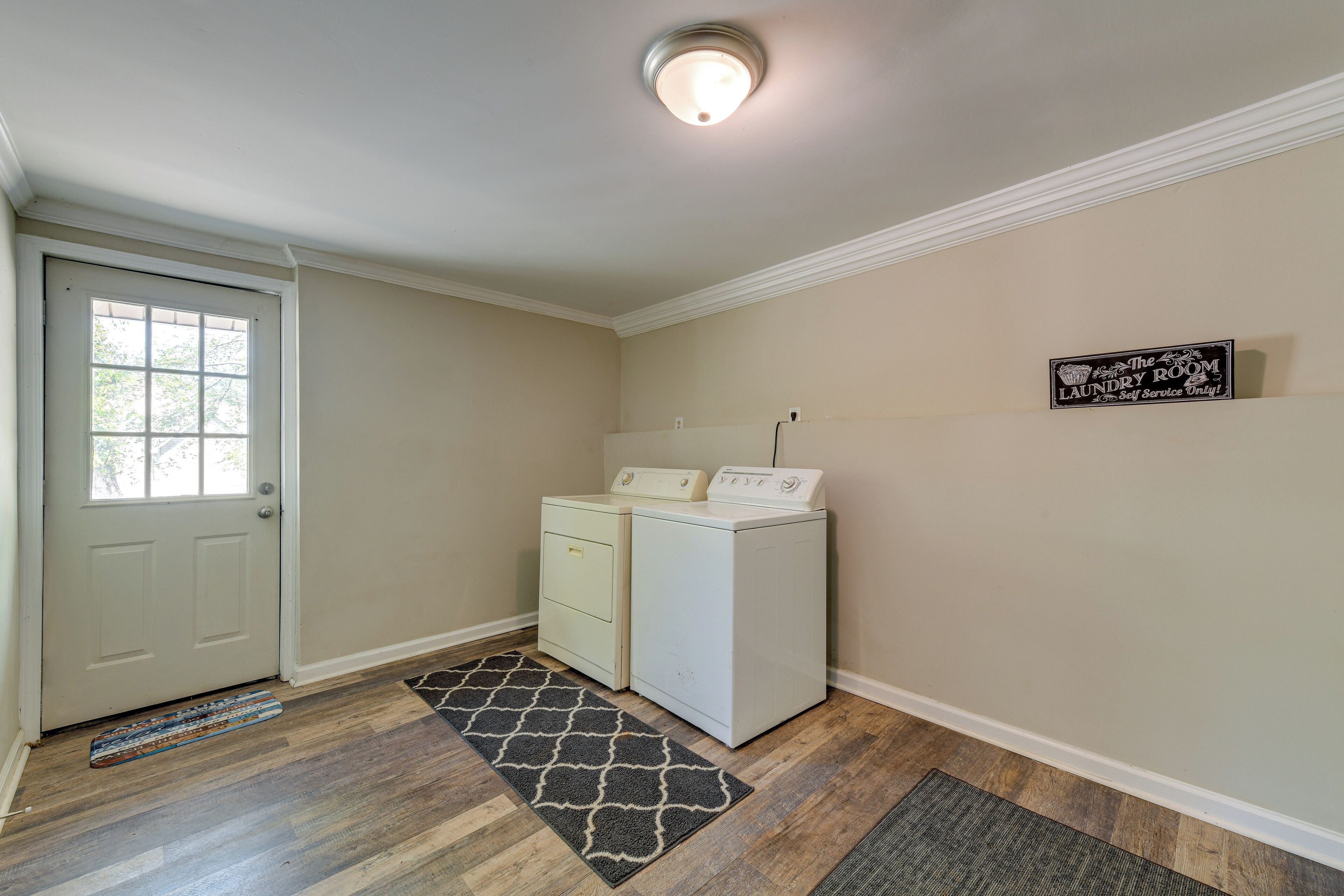 A laundry room with two white washers and dryers, a door, and a rug on the floor.