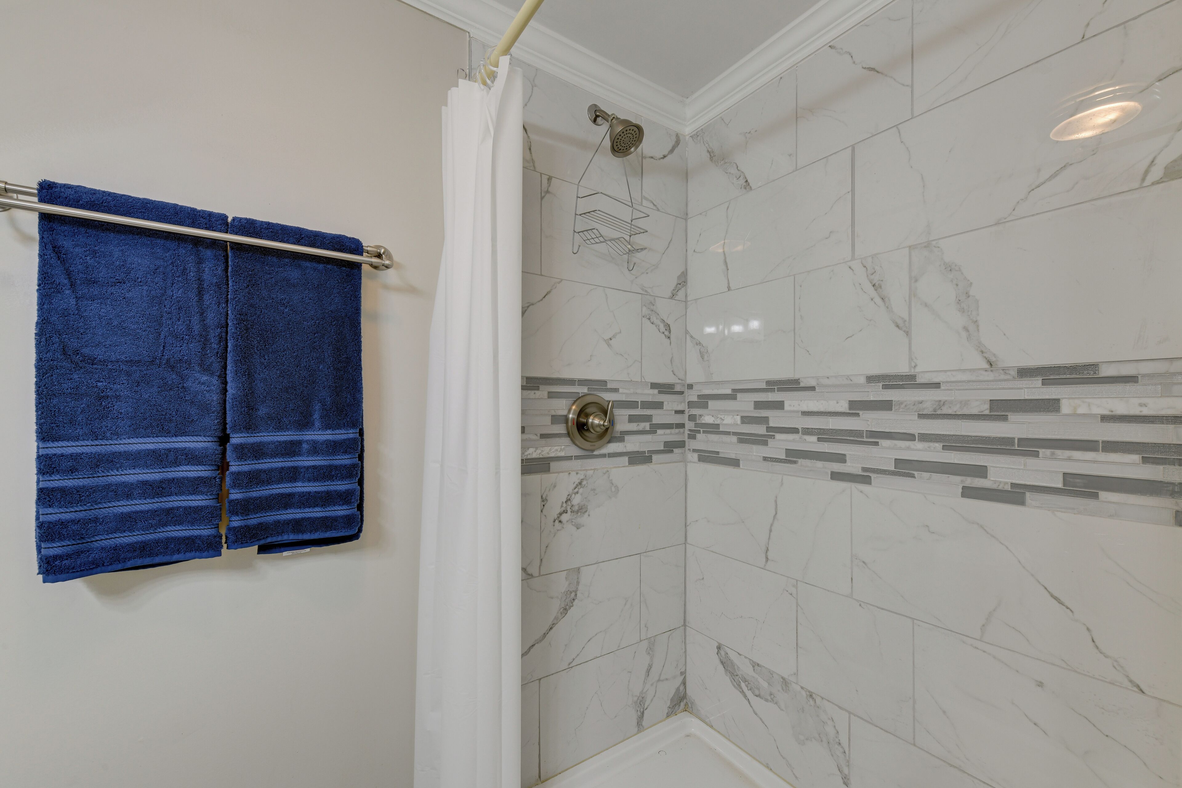 A bathroom with a shower, white marble tiles, a blue towel on a rack, and a showerhead.