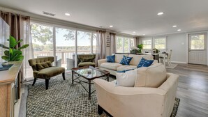 Ein großzügiges Wohnzimmer mit einem beige farbenen Sofa, einem grünen Sessel und einem Couchtisch. Ein großes Fenster bietet einen Blick ins Freie.