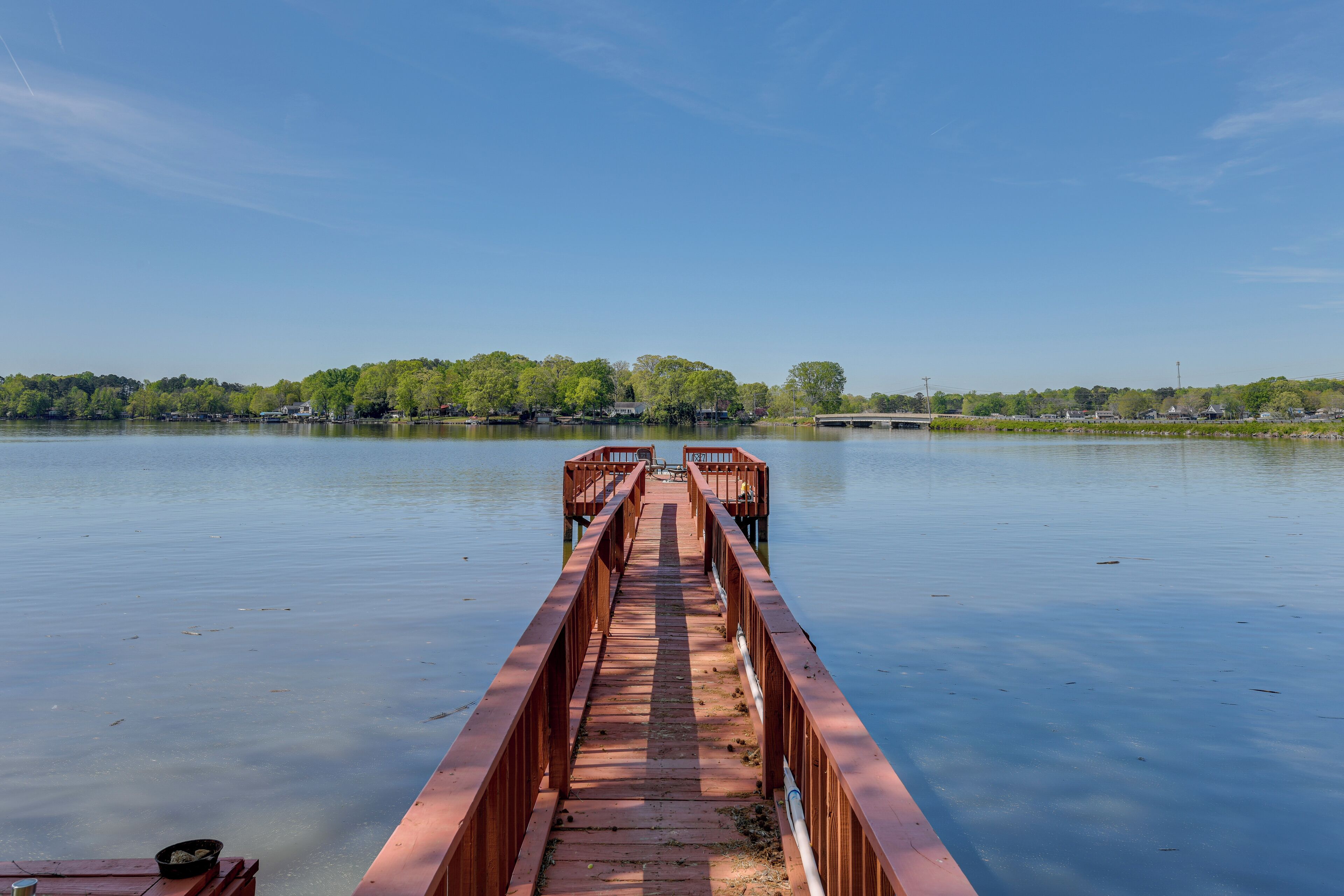 Une jetée en bois s’étendant dans une étendue d’eau calme, et menant à un quai où est amarré un bateau.