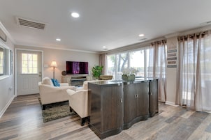 A modern living room with a beige sofa, a dark wooden entertainment center, and a large window with sheer curtains.