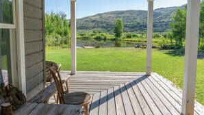 A wooden deck with a table and chairs, overlooking a grassy area and a body of water with hills in the background. - Tranquil Wyoming Cabin Near Uintas - 105 Acres! (Evanston)