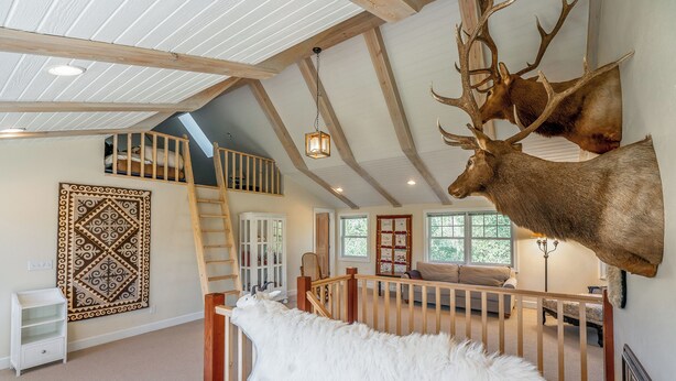 A spacious loft bedroom with a high ceiling, wooden beams, a skylight, a large window, and a mounted elk head. - Tranquil Wyoming Cabin Near Uintas - 105 Acres! (Evanston)
