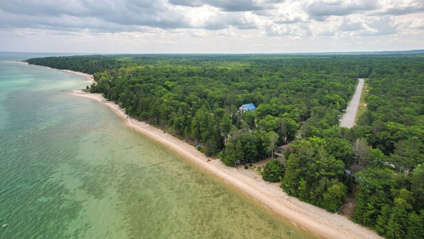 Ett flygbildsbild av ett kustområde med en strand, tät skog och en väg.