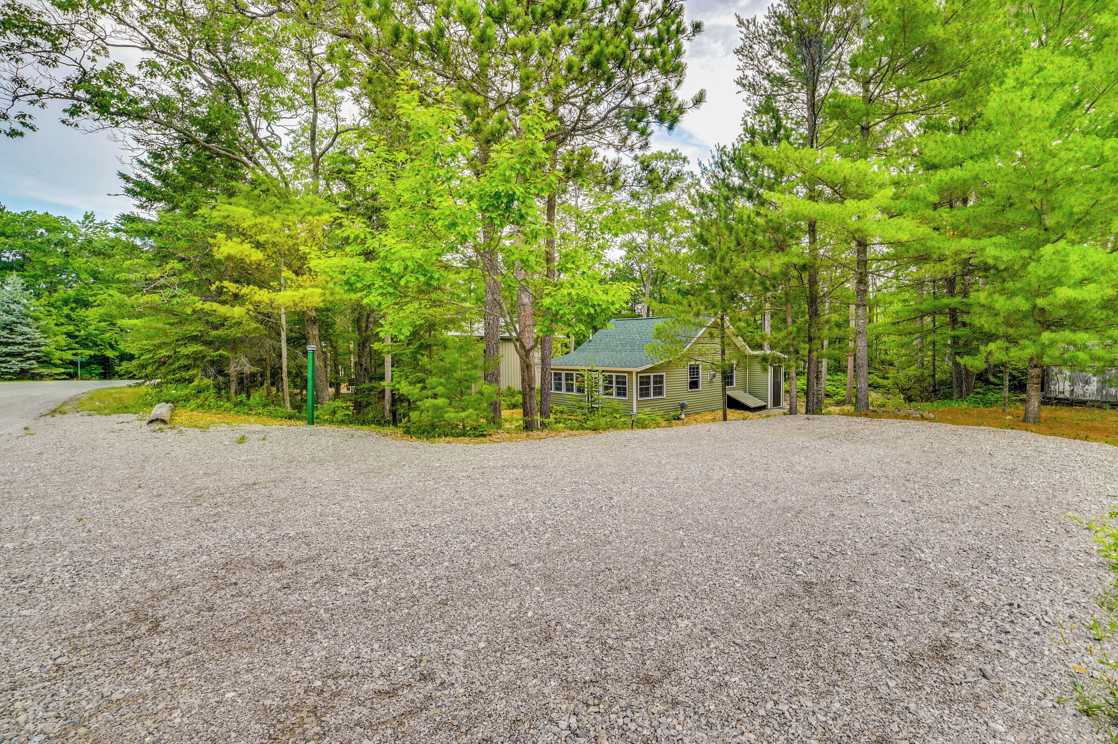 A house with a gravel driveway, surrounded by dense green trees.