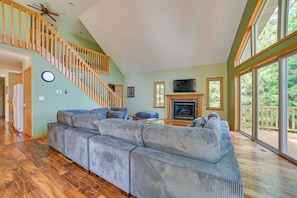A spacious living room with a large gray sectional sofa, a wooden staircase, and a fireplace. - Waterfront Lake Huron Getaway w/ Private Beach! (Rogers City)