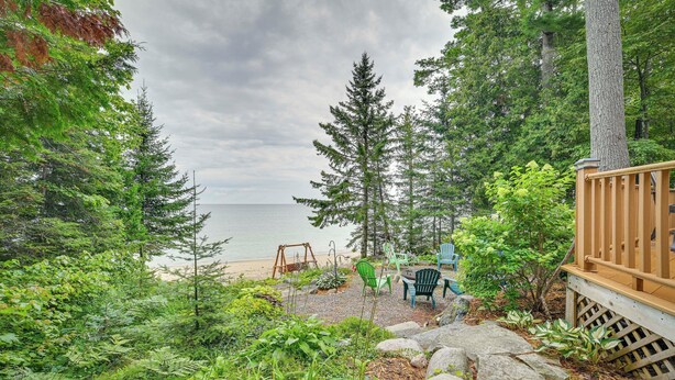 Une terrasse en bois avec une balançoire, des chaises et une vue sur la plage et l’océan.