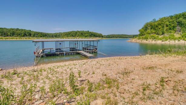 A dock extending into calm water, surrounded by a rocky shoreline and dense greenery. - Oakland Oasis: Serene Retreat in the Ozarks (Oakland)