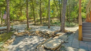 A rustic cabin surrounded by a forest with a stone fire pit and an American flag. - Oakland Oasis: Serene Retreat in the Ozarks (Oakland)