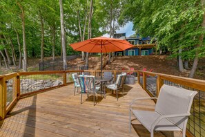 A wooden deck with a table and chairs, an umbrella, and a view of a house surrounded by trees. - Waterfront Troutman Vacation Rental on Lake Norman (Troutman)